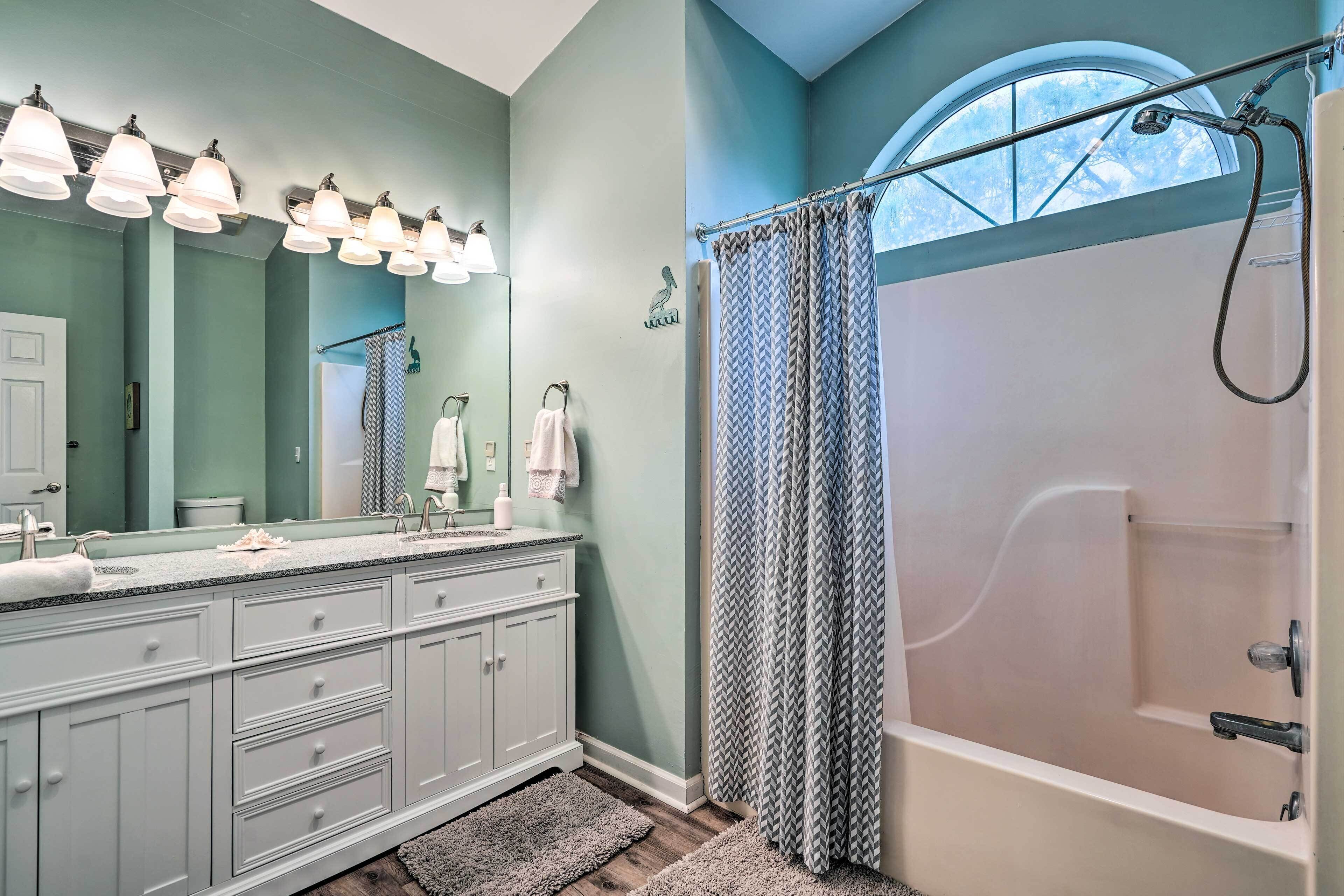 Une salle de bain dotée d’un grand meuble-lavabo, d’une douche avec une fenêtre incurvée et d’un luminaire encastré au plafond.