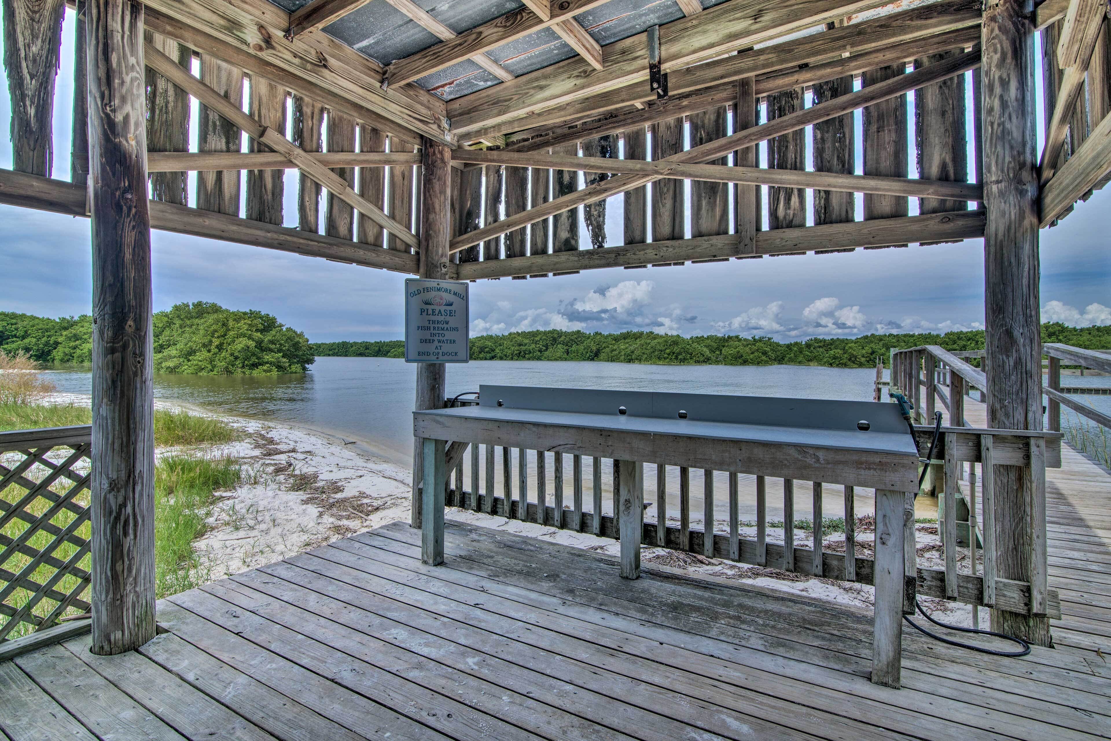 A wooden pier with a bench, a sign warning about deep water, and a view of a lake surrounded by greenery.