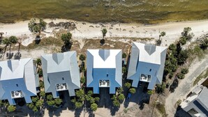 Een groep moderne gebouwen met platte daken, gelegen nabij een strand met zichtbaar zand en schaarse begroeiing.