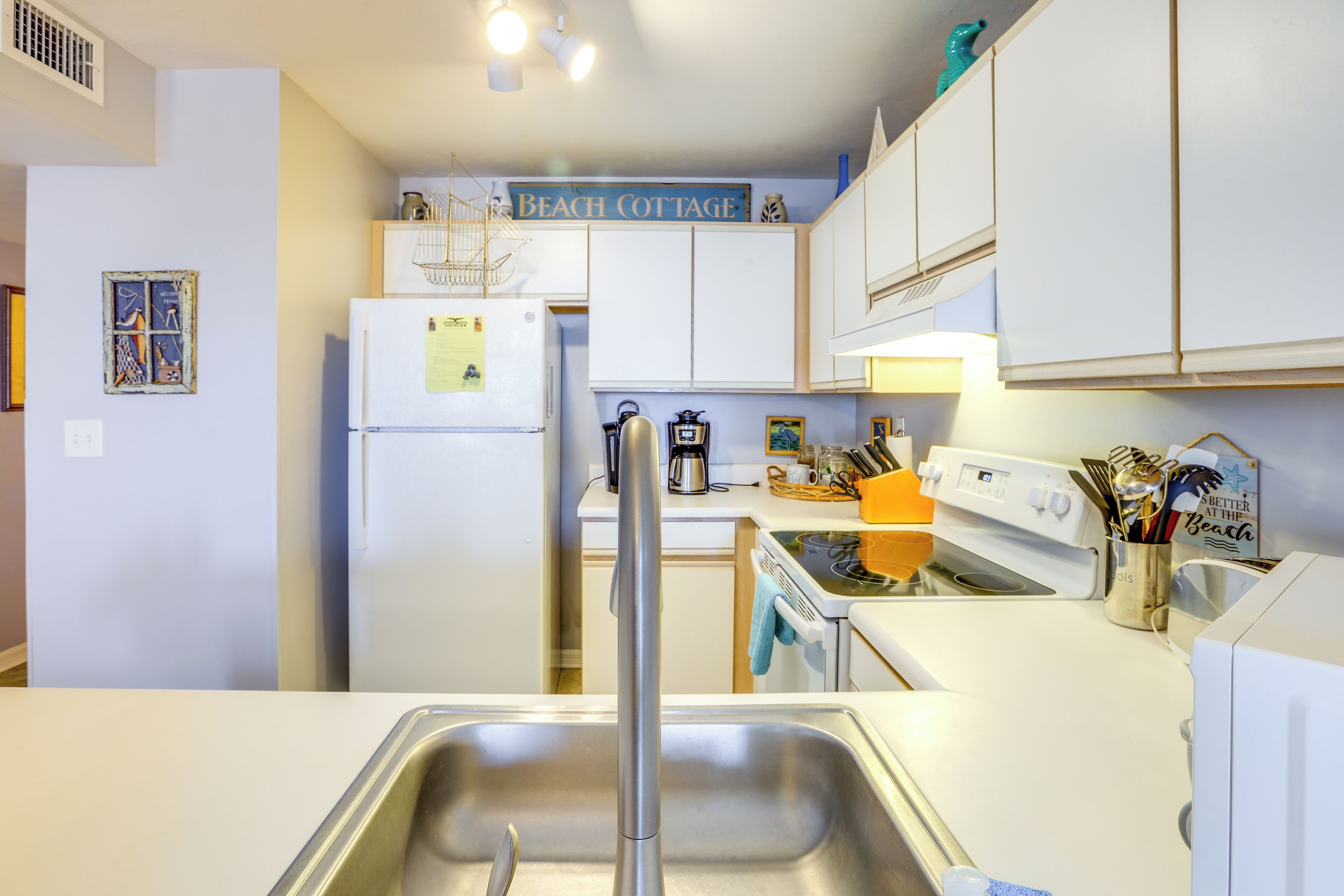 A compact kitchen with white cabinets, a stainless steel sink, a refrigerator, and a coffee maker.