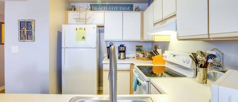 A compact kitchen with white cabinets, a stainless steel sink, a refrigerator, and a coffee maker.