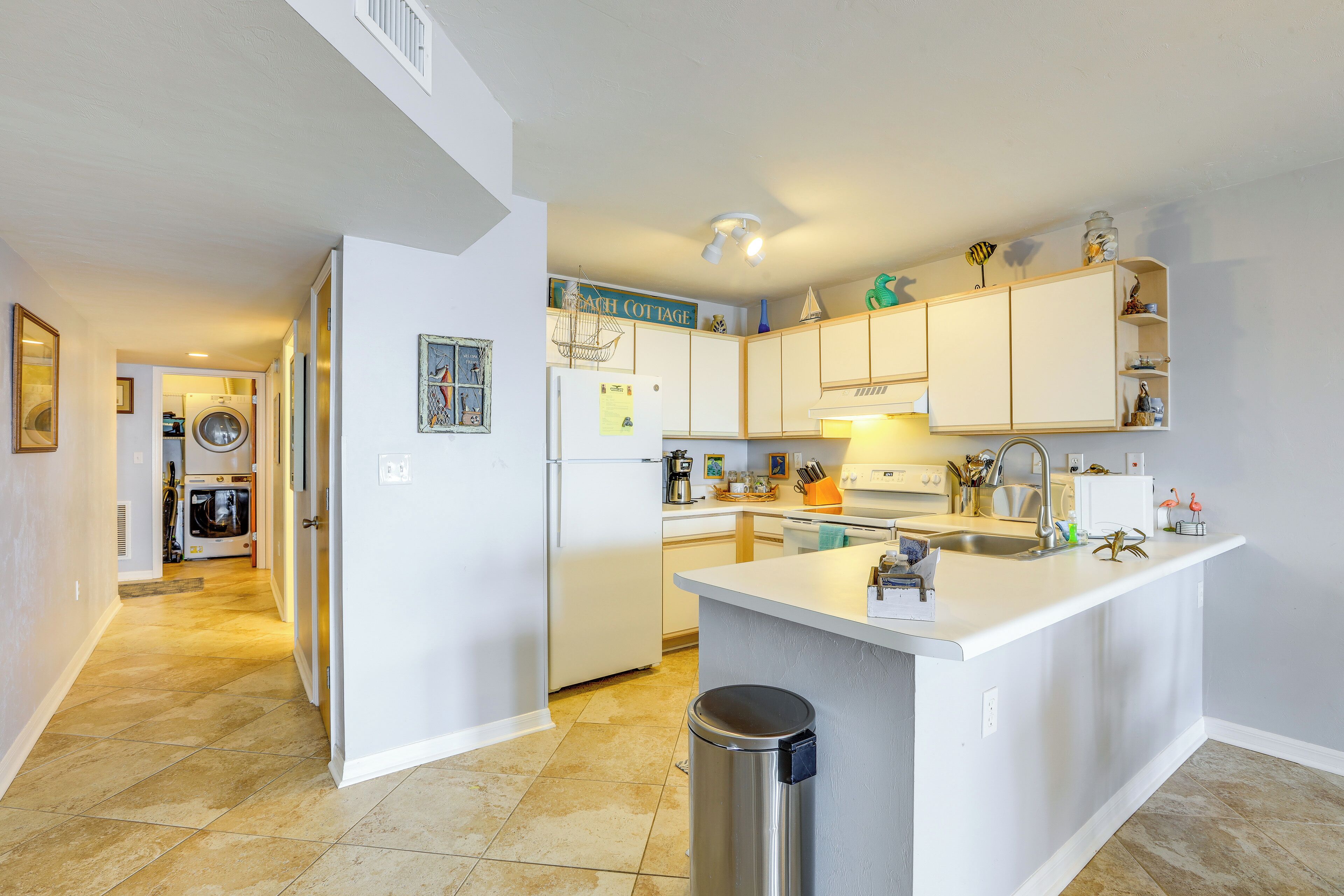 A modern kitchen with white cabinets, a central island, and a view into the laundry area.