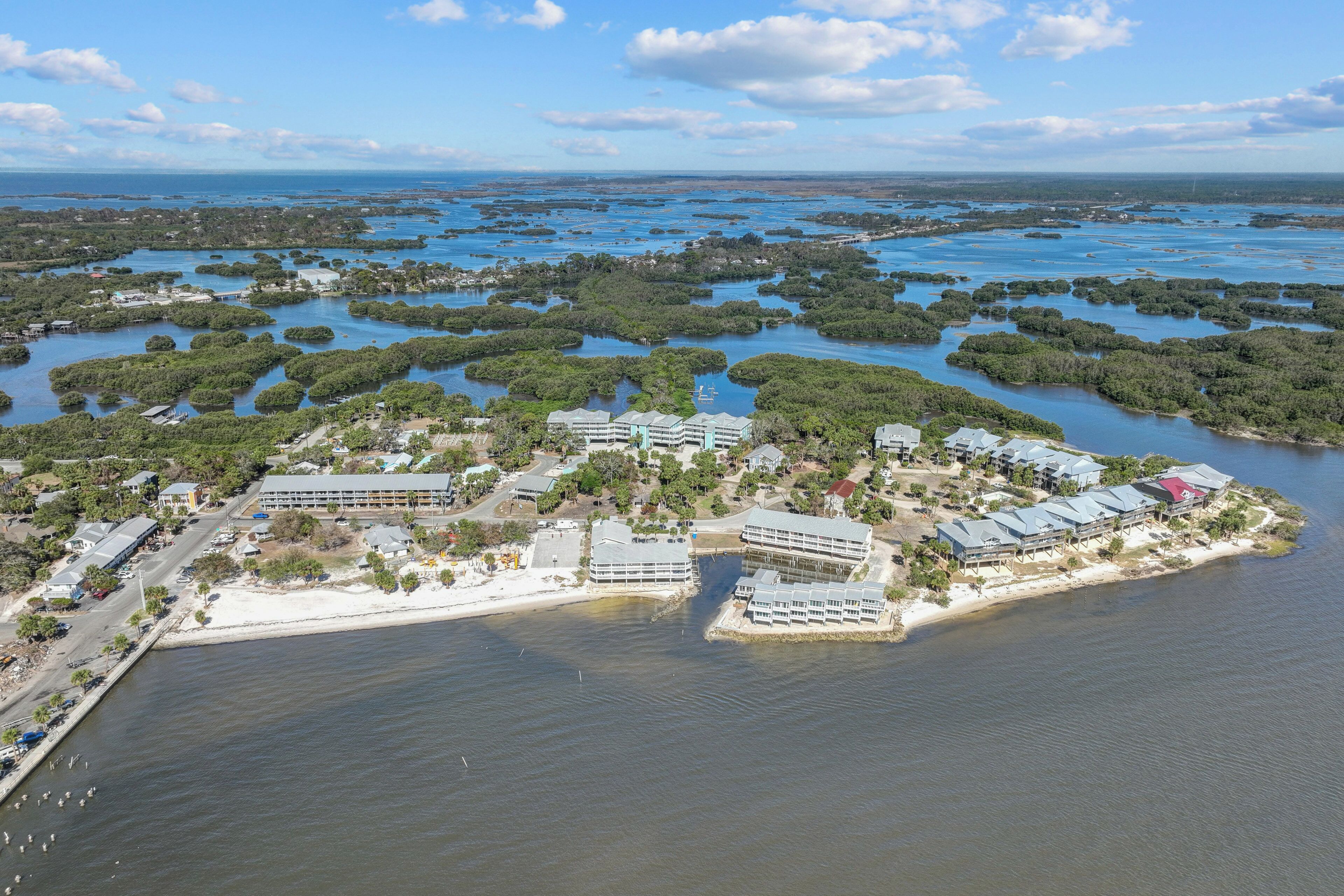 An aerial view of a coastal resort with multiple buildings, a beach, and a mangrove-filled bay.