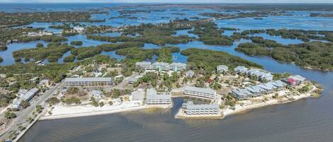 An aerial view of a coastal resort with multiple buildings, a beach, and a mangrove-filled bay.