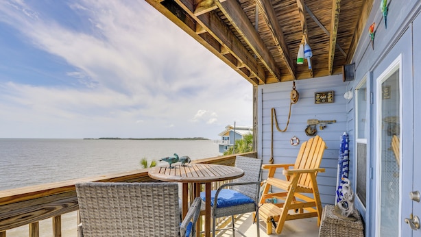 Een houten terras met rieten stoelen en een tafel met uitzicht op een waterpartij.