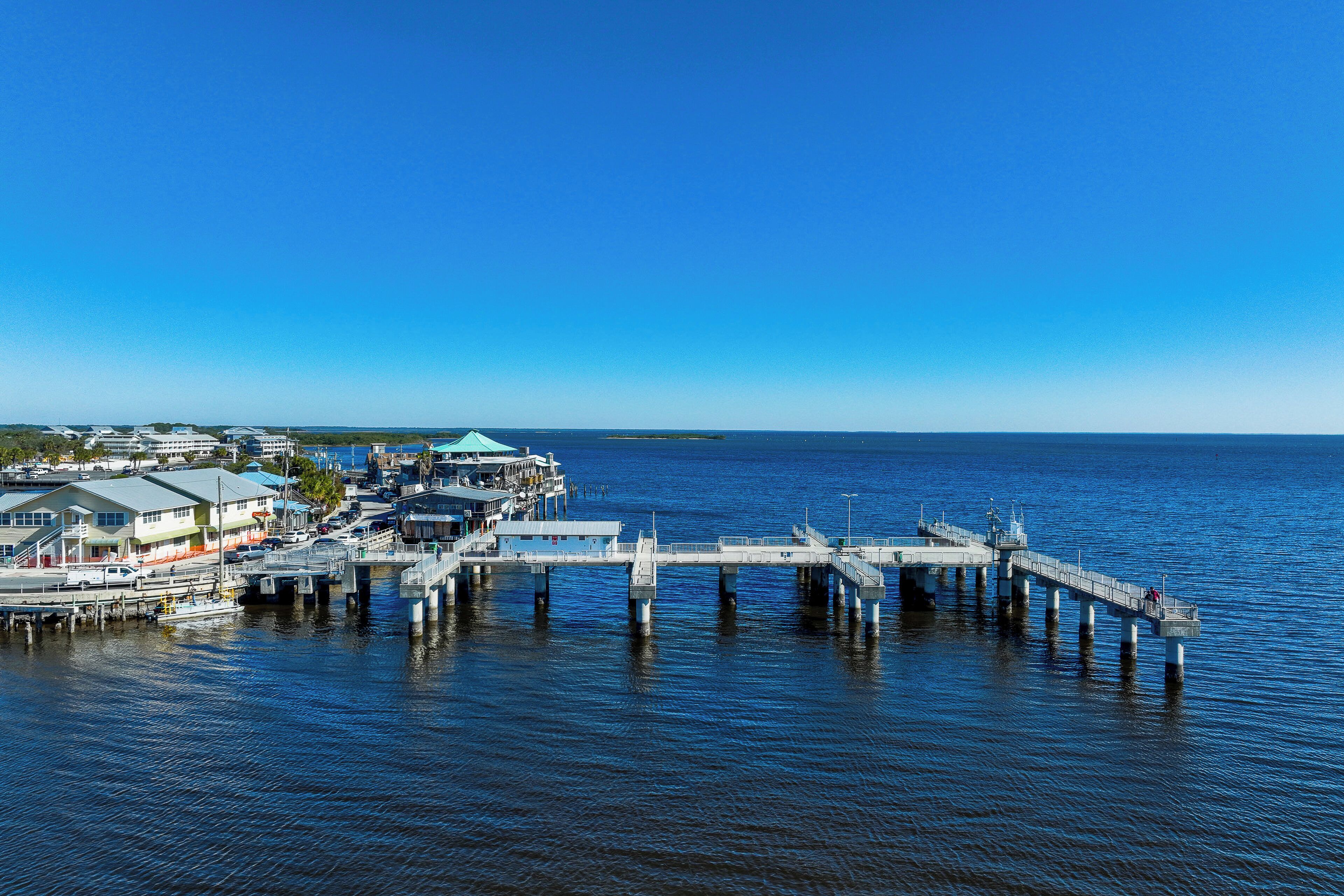 A pier extending into calm waters with buildings and a dock on the left.