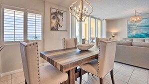 A dining area with a wooden table, upholstered chairs, a chandelier, and artwork on the walls. - Beachfront Fort Walton Beach Condo w/ Pool Access! (Fort Walton Beach)