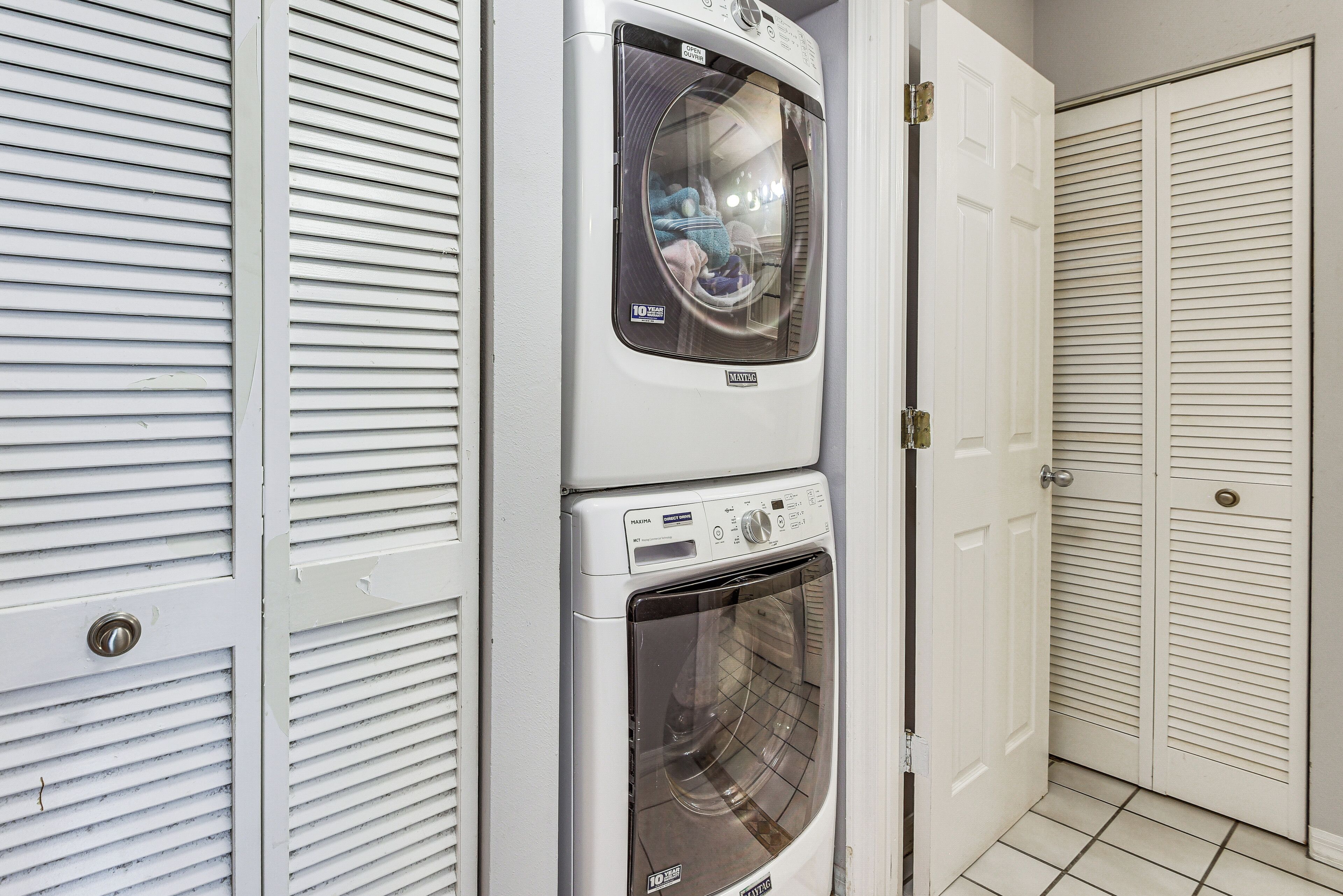 A laundry area with two stacked washing machines and a dryer, enclosed by white doors with horizontal louvered panels.