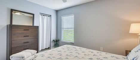 A bedroom with a bed, a dresser, a mirror, a ceiling fan, and a window with blinds.