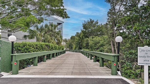 A wooden bridge with green railings leading to a building with a sign indicating 'The Cove at Sandy Point 3601 PRIVATE PROPERTY'.