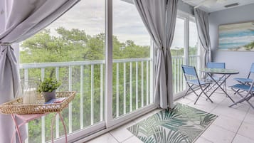 A balcony with a view of trees, a ceiling fan, and a table with chairs.