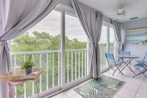Un balcon avec vue sur les arbres, un ventilateur de plafond et une table avec des chaises.