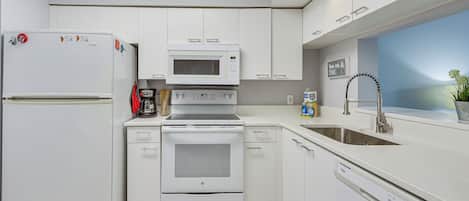 Een moderne keuken met witte kastjes, een ingebouwde magnetron, oven en vaatwasser.