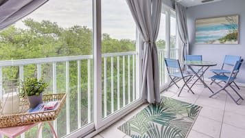 A balcony with a view of trees, a table with chairs, and a ceiling fan.
