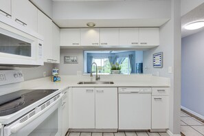 A modern kitchen with white cabinetry, a built-in microwave, an oven, a dishwasher, and a window with curtains.