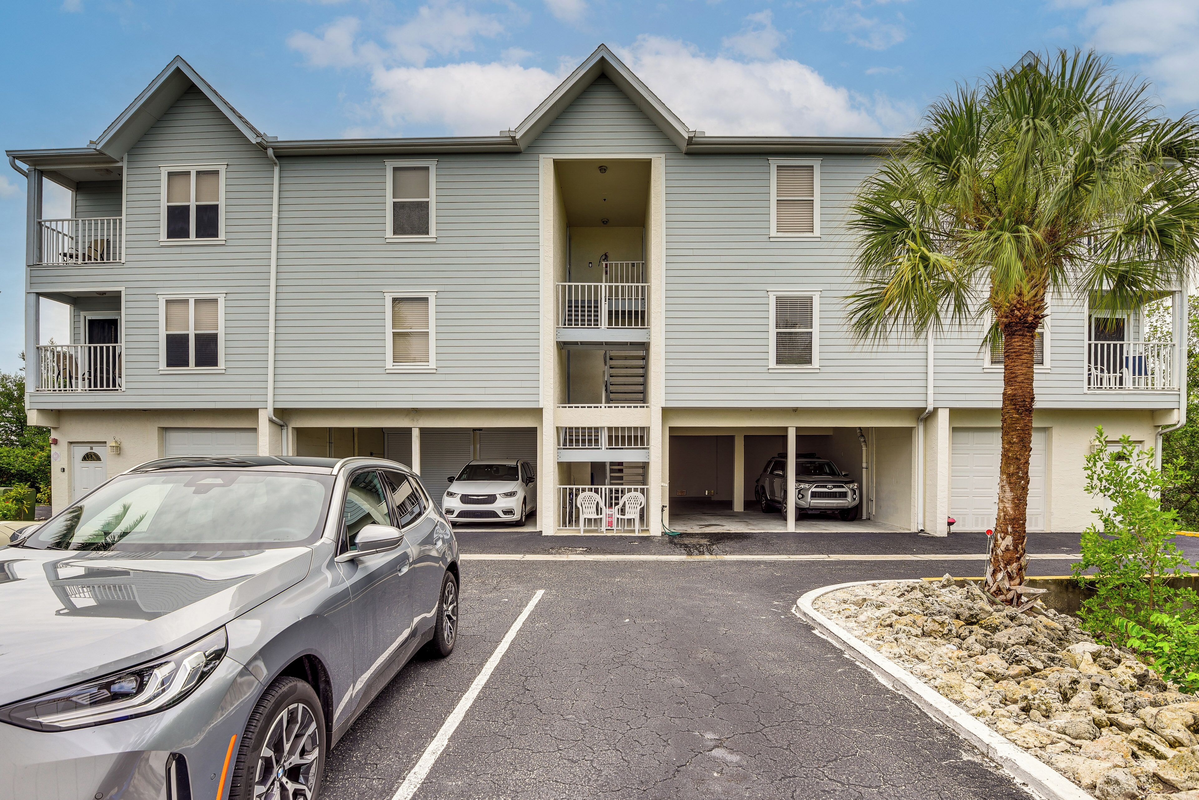 A multi-story building with a central entrance, parking spaces, and a palm tree.