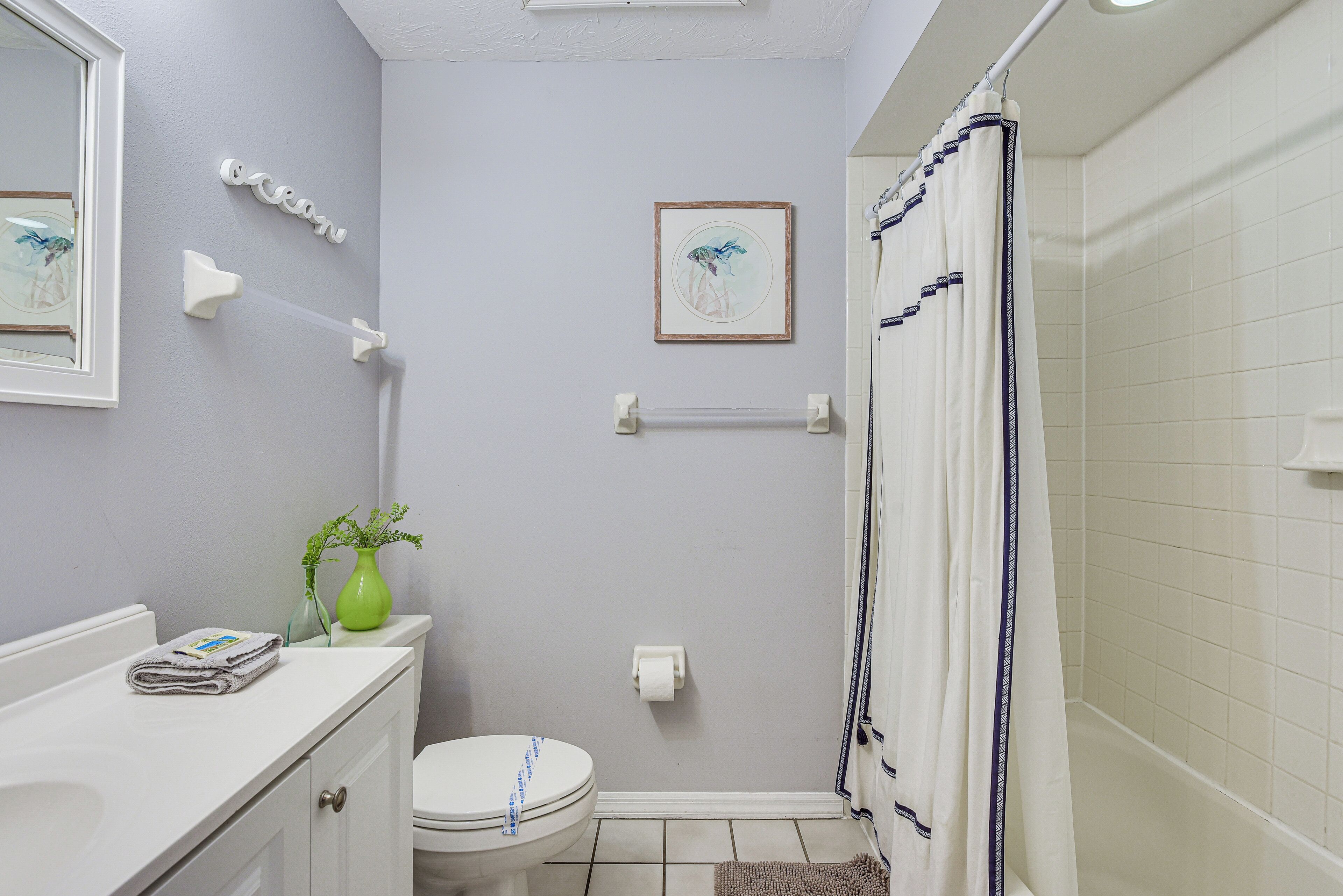 A bathroom with a toilet, a shower with a curtain, a sink with a mirror, and a framed picture on the wall.
