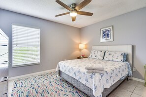 A bedroom with a bed, a ceiling fan, a bedside lamp, a framed picture on the wall, and a patterned rug.