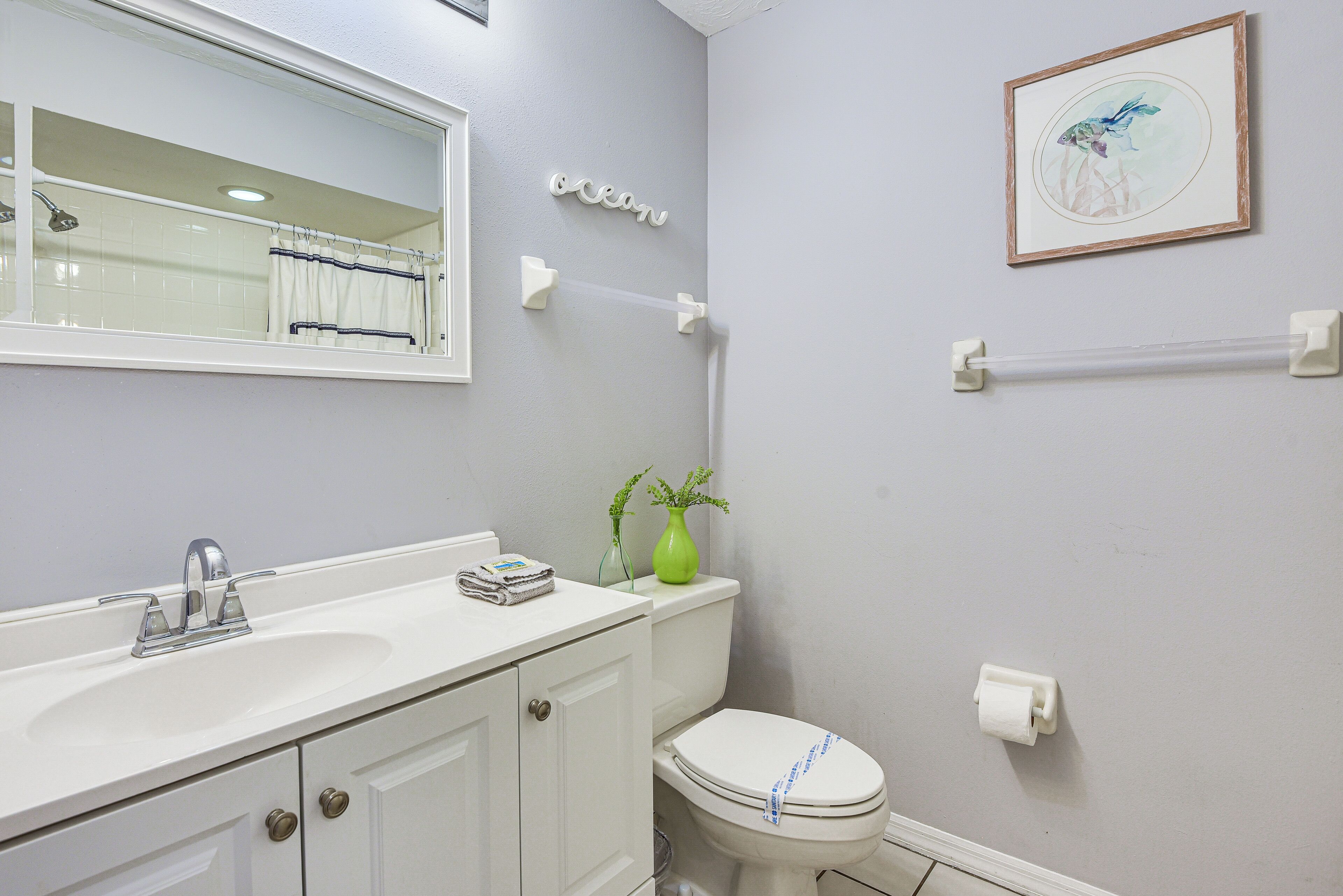 A bathroom with a white sink, mirror, toilet, and a framed picture on the wall.