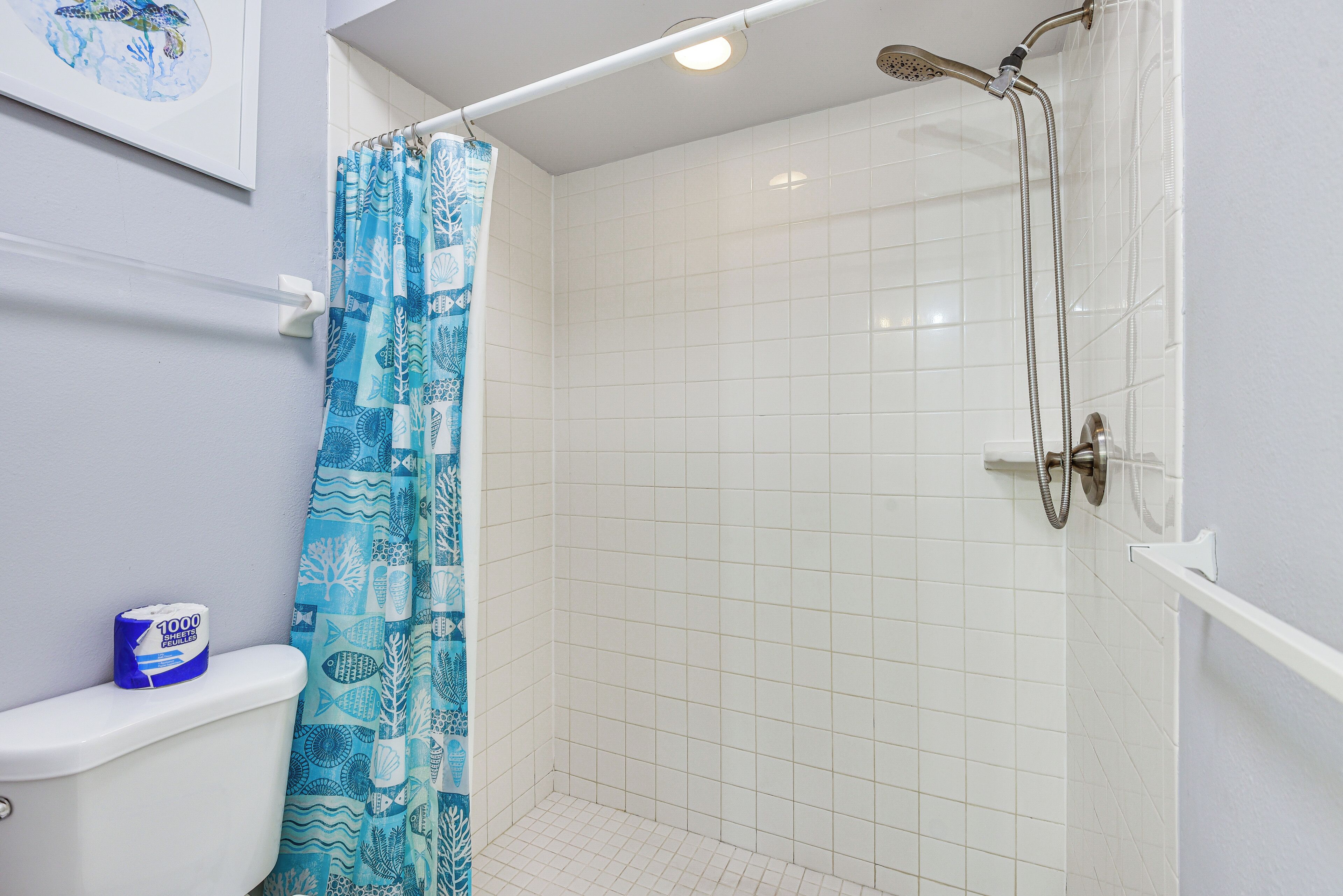 Ein Badezimmer mit Dusche, weißen Fliesen, einem blauen Duschvorhang mit Meeresmotiv und einer Toilette mit Toilettenpapier.
