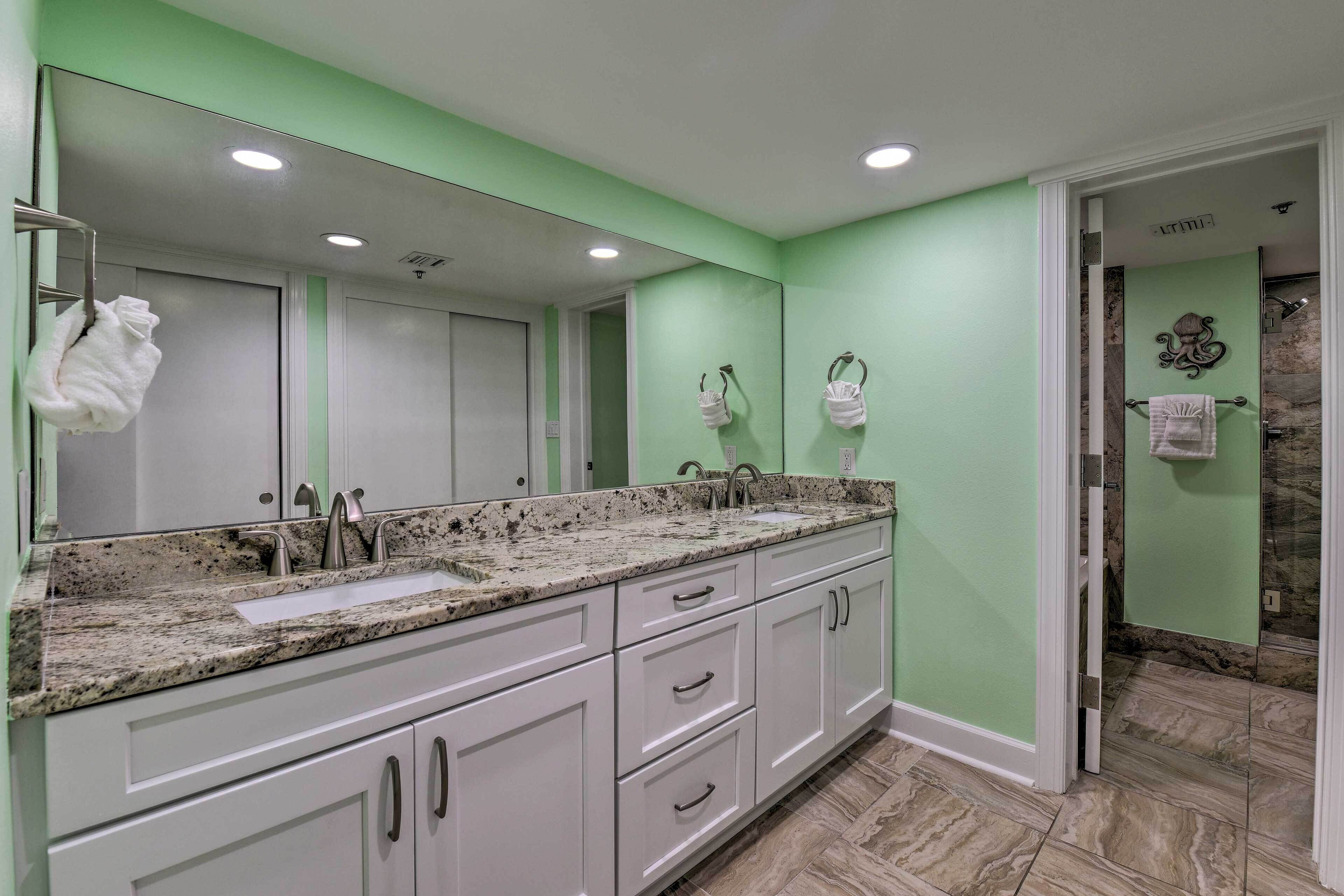A bathroom with a granite countertop sink, white cabinets, and a green wall.