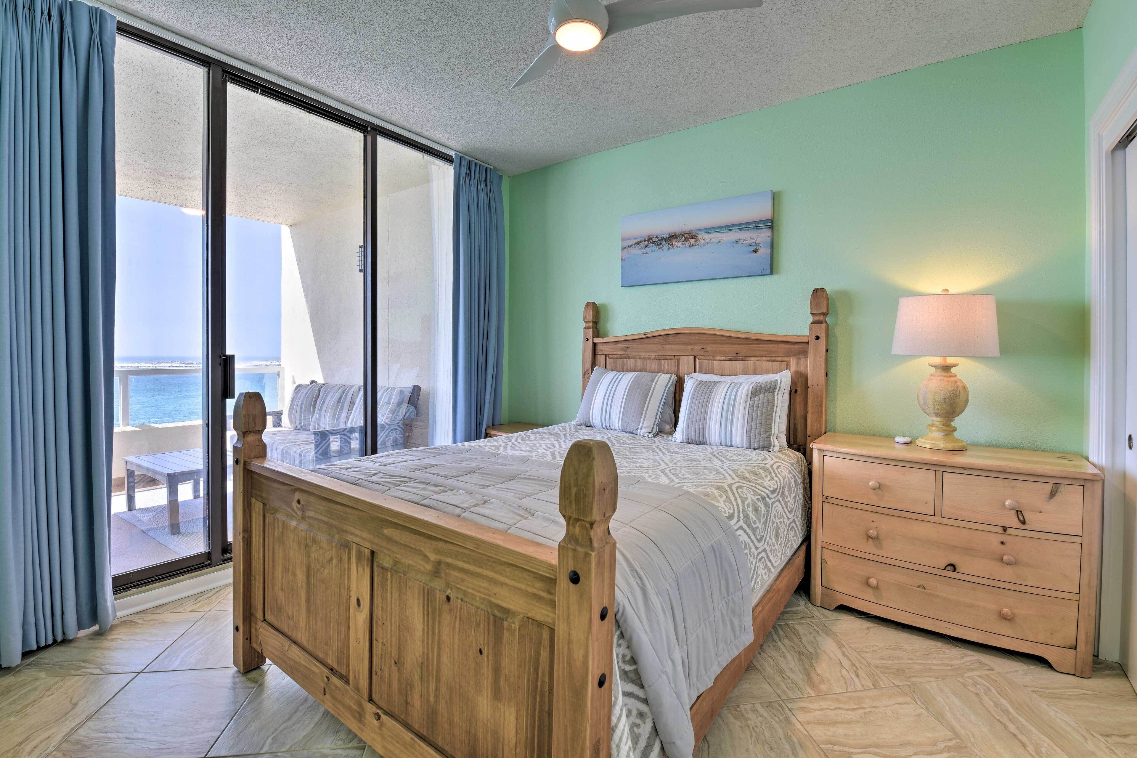 A bedroom with a wooden bed, a nightstand with a lamp, and a view of the ocean through a sliding door.