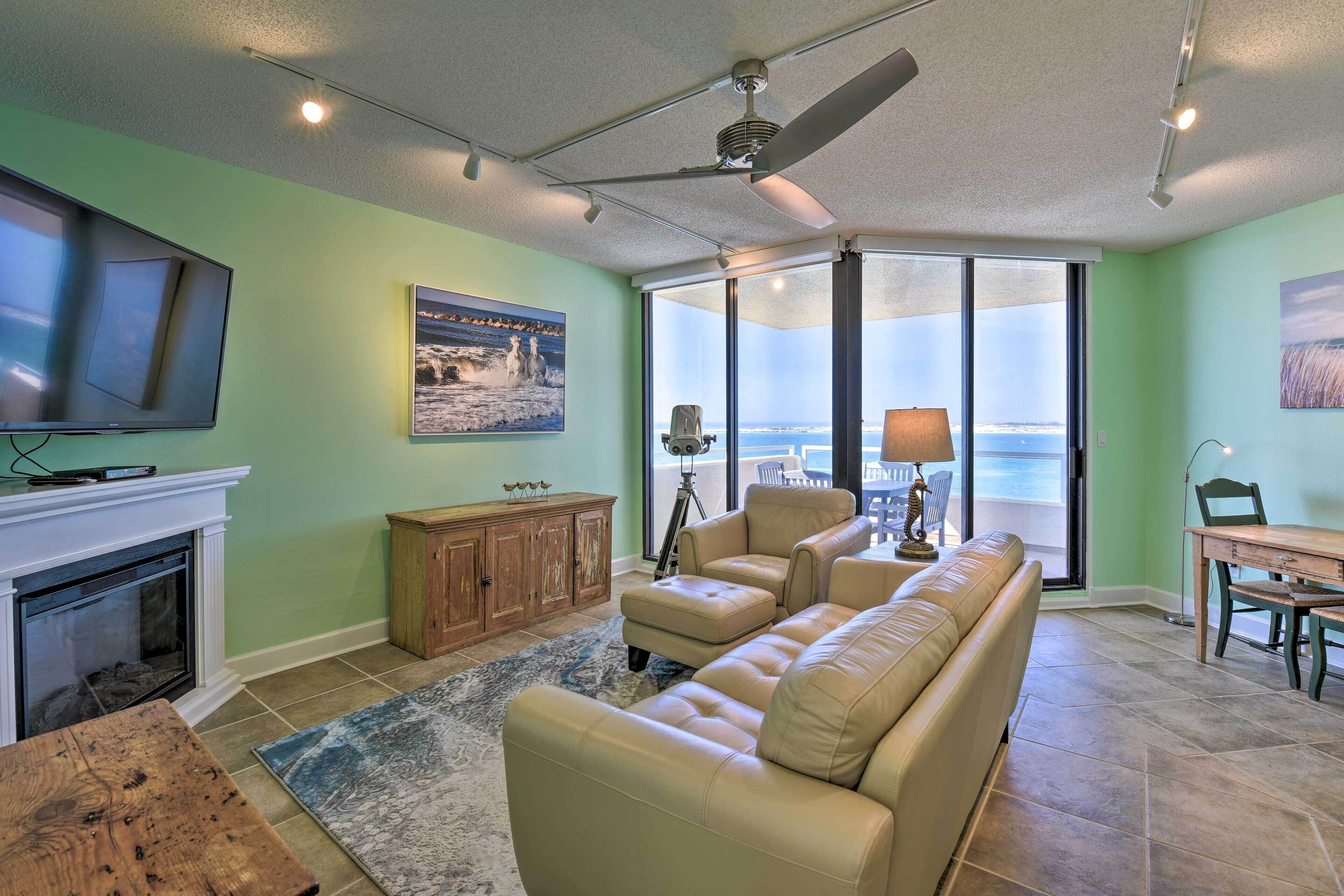A living room with a fireplace, a large window, and a view of the ocean.