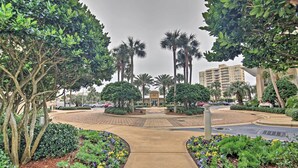 A landscaped area with a central pathway, surrounded by various plants and trees, leading to a building entrance. - Beachfront Destin Condo w/ Pool & Harbor View! (Destin)