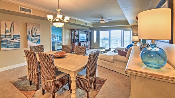 A dining area with a wooden table and woven chairs, a chandelier, and artwork on the walls. - Beachfront Destin Condo w/ Pool & Harbor View! (Destin)
