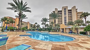 A swimming pool with blue lounge chairs, palm trees, and a large hotel building in the background. - Beachfront Destin Condo w/ Pool & Harbor View! (Destin)