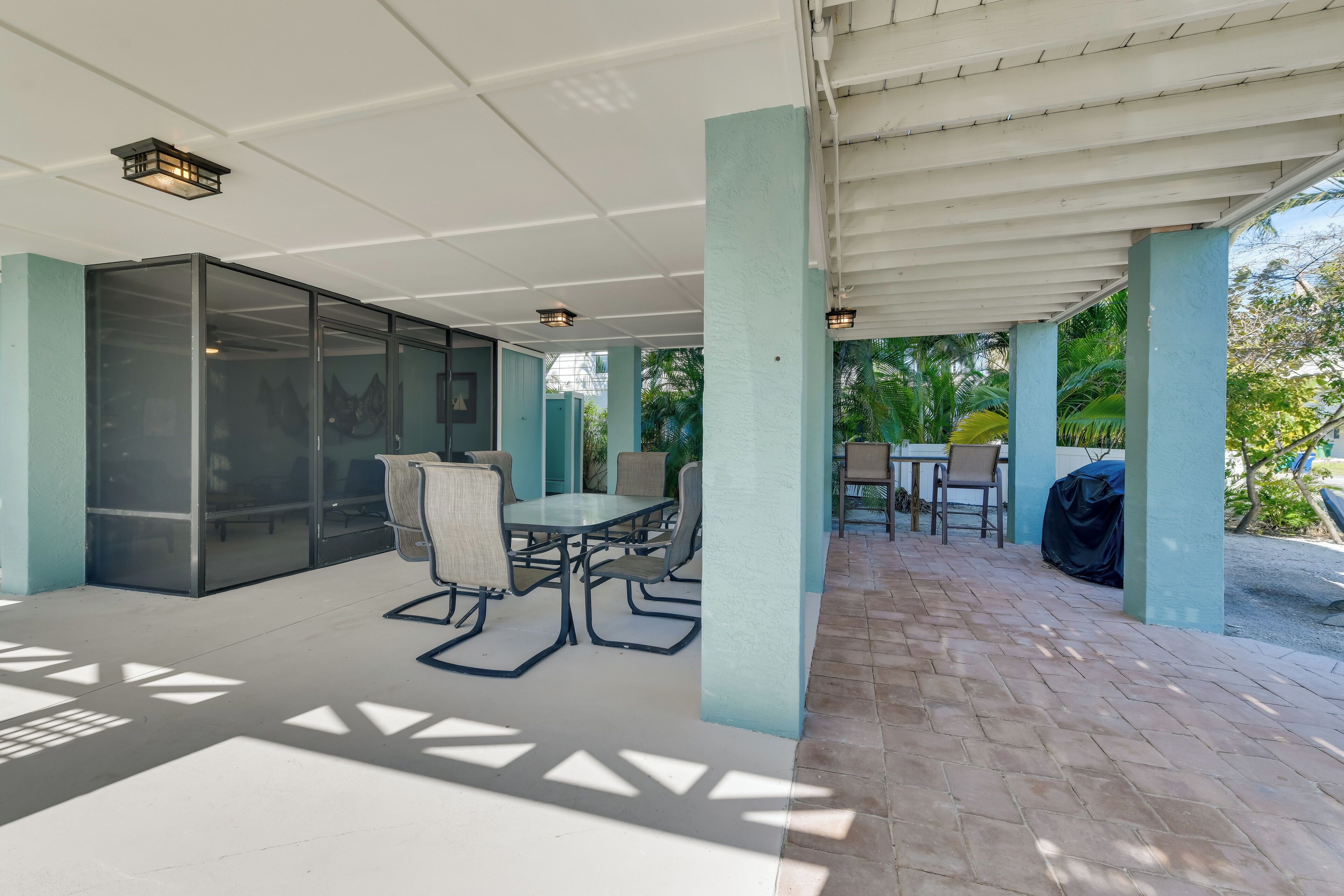 Un patio exterior con cerramiento de vidrio, una mesa con sillas y una parrilla.