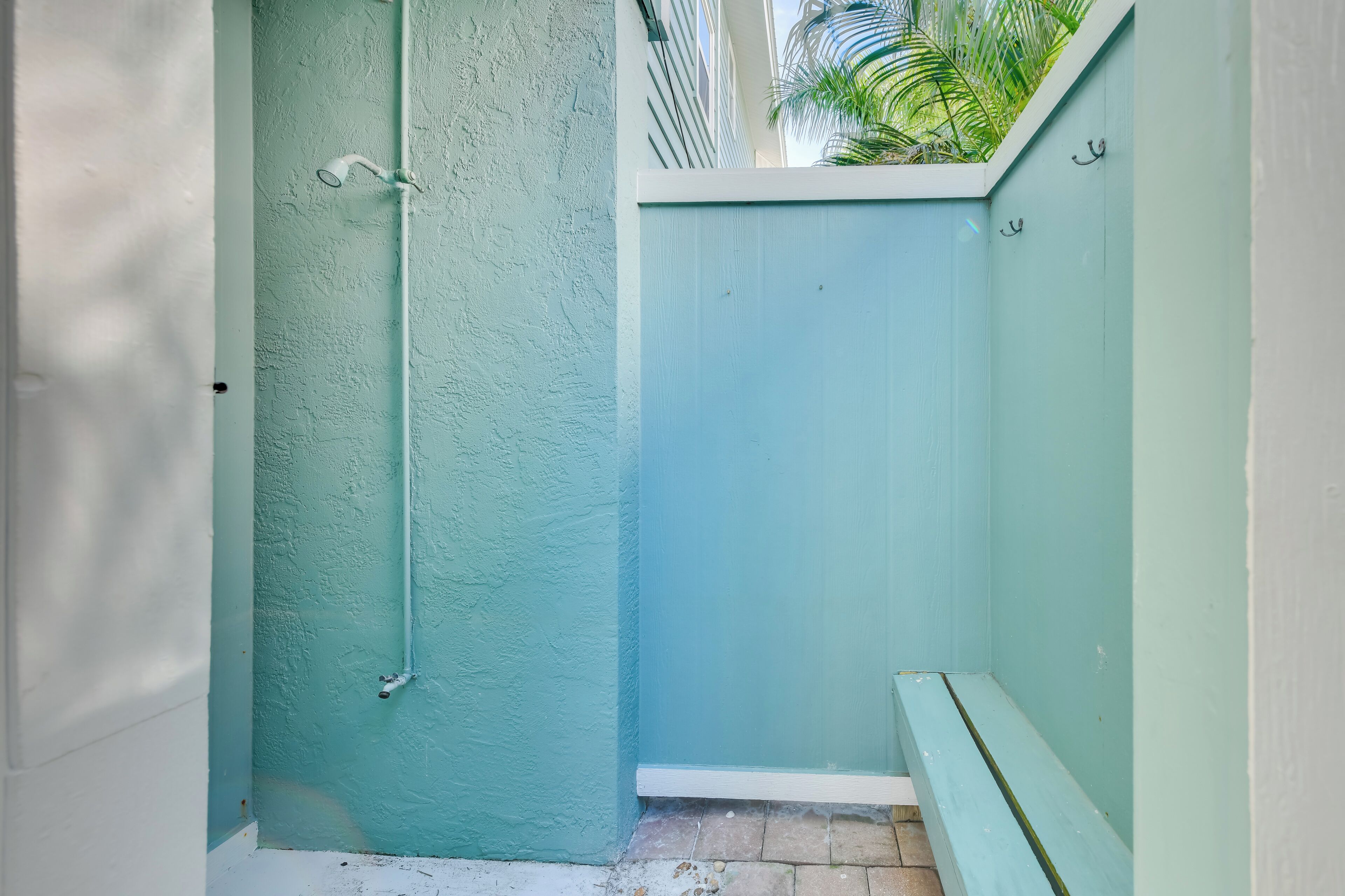 Un baño pequeño y cerrado con puerta y paredes color turquesa, un banco y una zona de ducha visible.