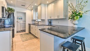 A modern kitchen with white cabinetry, granite countertops, and a central island with stools. - Steps to Ocean & Bay: Bradenton Beach Townhome! (Bradenton Beach)
