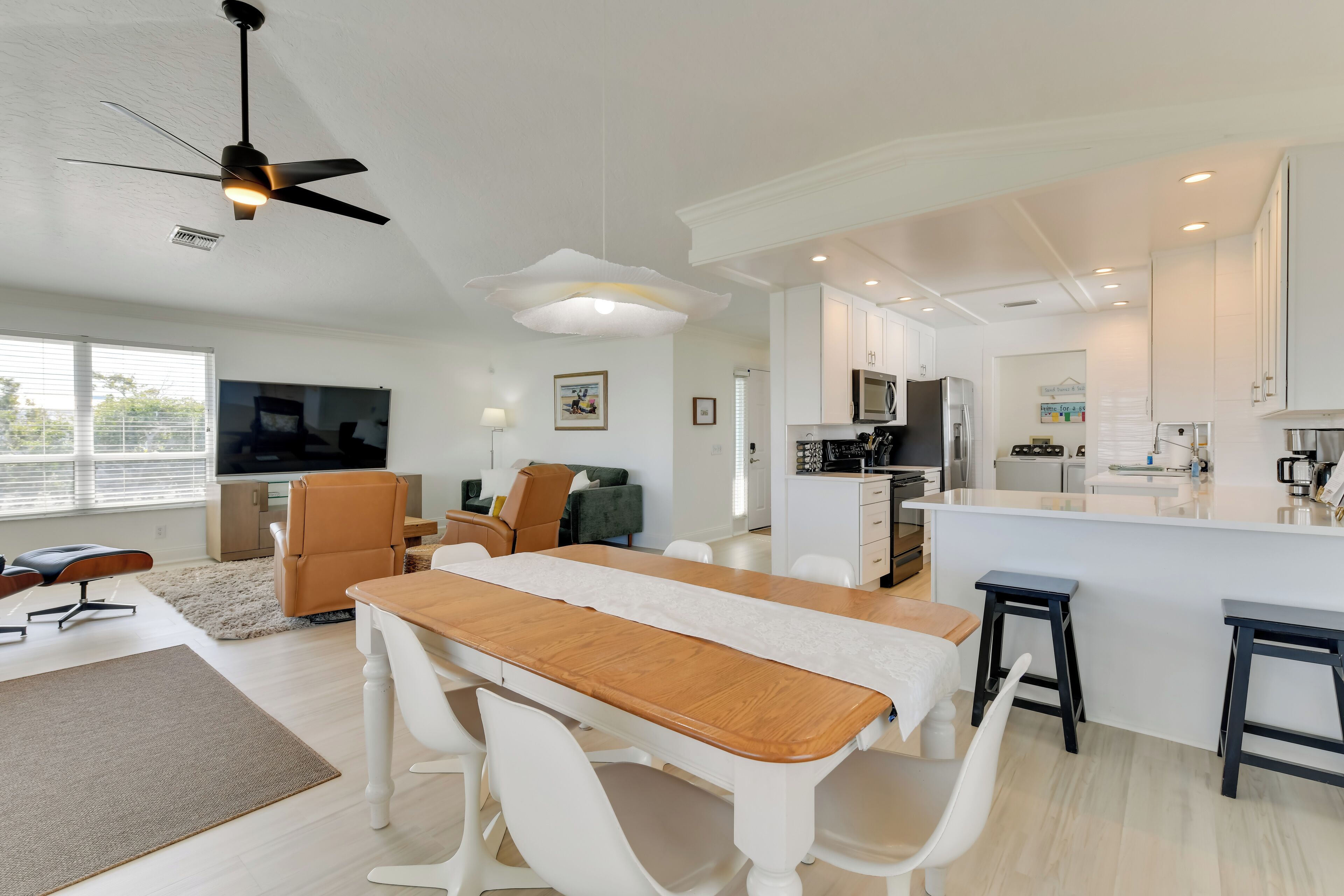 Uma cozinha moderna com armários brancos, uma ilha central e um espaço de jantar com mesa de madeira e cadeiras brancas.