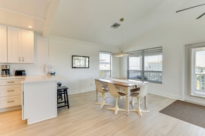 Una cocina moderna con armarios blancos, una isla central y una zona de comedor con mesa y sillas de madera.