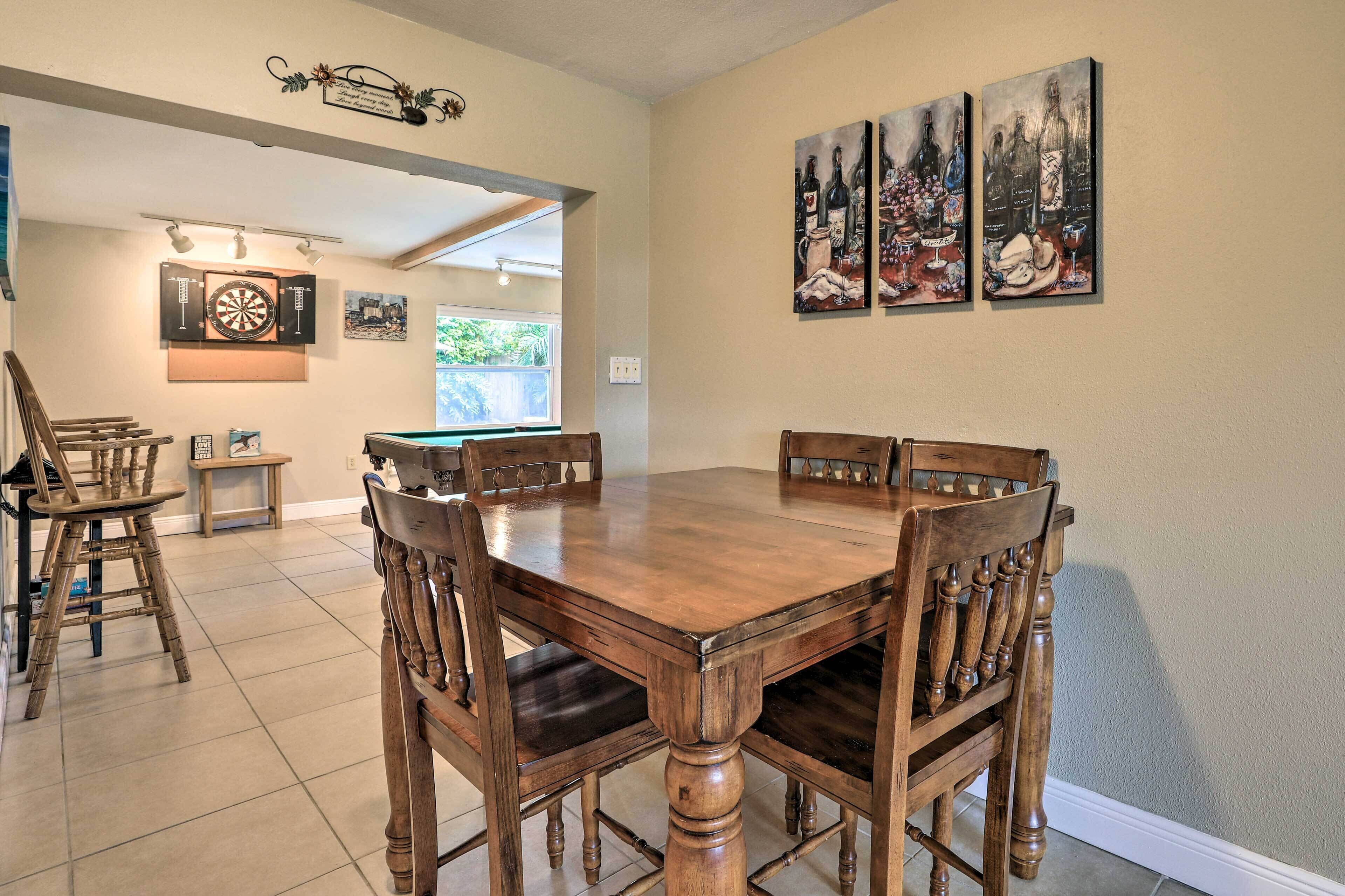 Un espace repas avec une table et des chaises en bois, un jeu de fléchettes et des œuvres d’art murales.