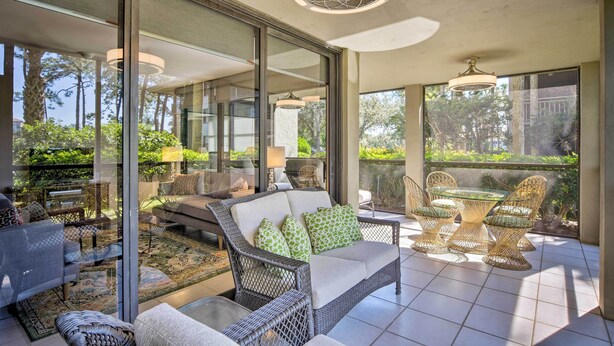 A modern outdoor patio with wicker furniture, glass doors, and large windows offering views of greenery.