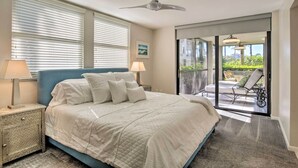 A bedroom with a bed, bedside lamps, a ceiling fan, and a view of an outdoor patio with a chair and table.