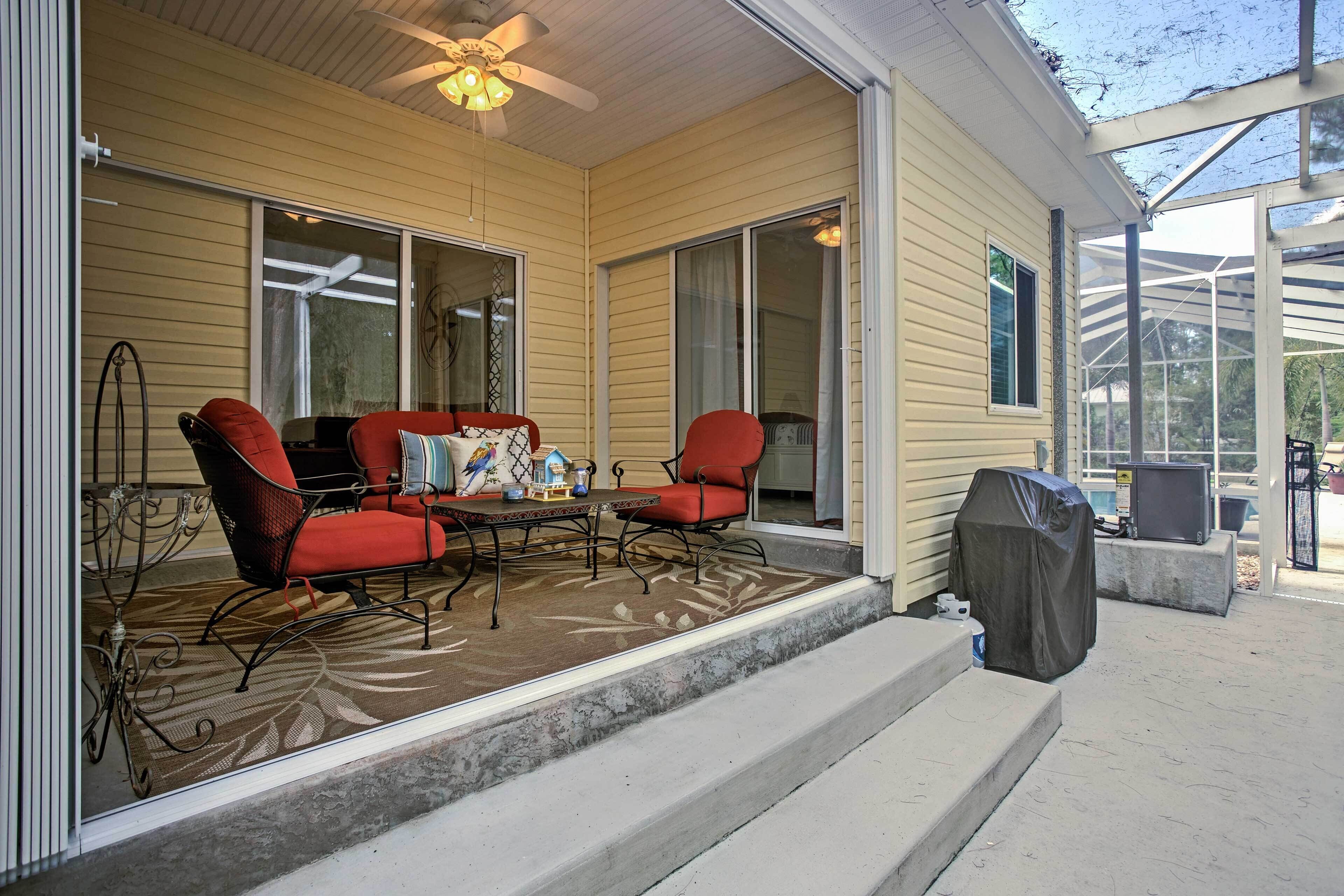 A covered patio with a ceiling fan, two red chairs, a table, and a grill.