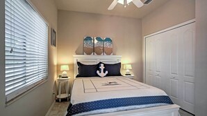 A bedroom with a bed, a ceiling fan, a nightstand, a lamp, and a door. - Bokeelia Cottage w/ Private Pool (Bokeelia)