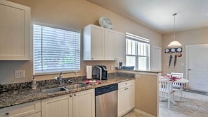 A kitchen with white cabinets, a granite countertop, a dishwasher, and a dining area with a table and chairs. - Bokeelia Cottage w/ Private Pool (Bokeelia)