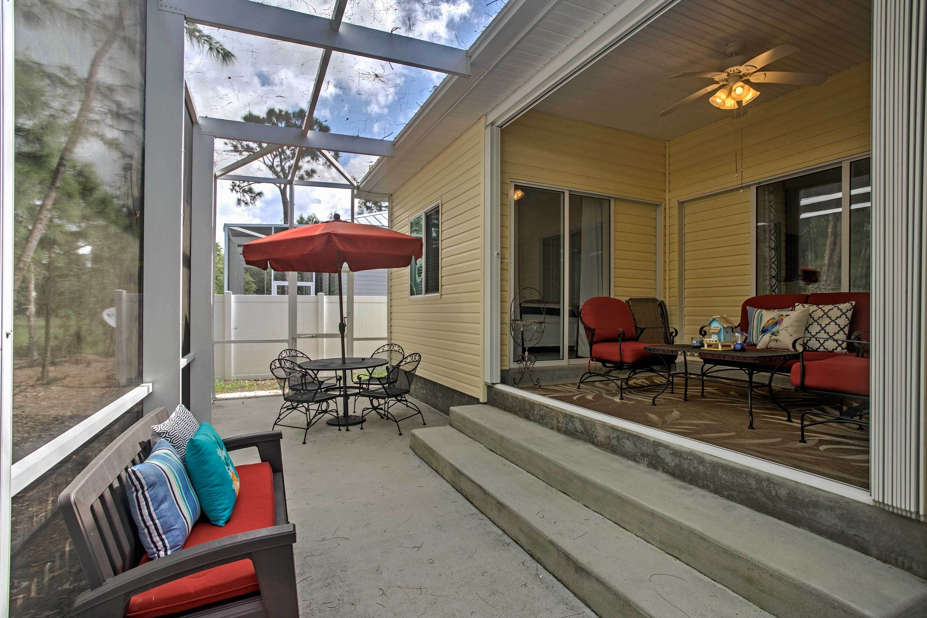 A covered patio with outdoor furniture, including a table and chairs, and a sofa with a red cushion.