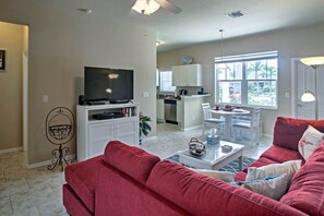 A living room with a red sofa, a flat-screen TV, and a dining area with a table and chairs.