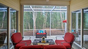 A covered patio with two red chairs, a small table, and a sofa with cushions. - Bokeelia Cottage w/ Private Pool (Bokeelia)