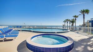 A pool area with blue lounge chairs and a hot tub, surrounded by palm trees and a clear sky. - Beautiful Daytona Beach Shores Condo w/ Hot Tub! (Daytona Beach Shores)