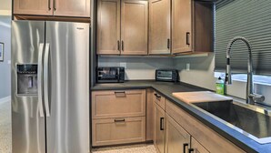 A kitchen with wooden cabinets, a stainless steel refrigerator, a microwave, a toaster, and a sink.