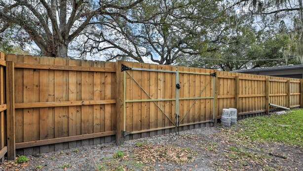 A wooden fence with a gate, a tree, and some grass and leaves on the ground.