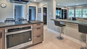 A modern kitchen with a built-in oven, a stainless steel range hood, and a bar area with bar stools.