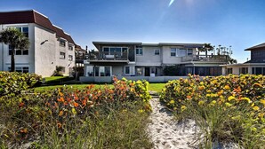 Uma propriedade à beira-mar com vários edifícios, um caminho de areia e diversas plantas floridas.