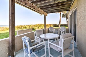Ein überdachter Patio-Bereich mit einem runden Tisch und vier Stühlen, mit Blick auf einen angelegten Garten und das Meer.